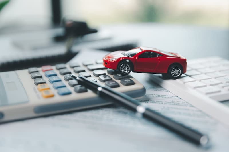電卓の上に置かれた赤いミニカーとペンで正確なお見積りのイメージ