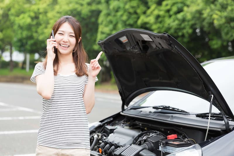 ボンネットを開けた車の前で電話をする笑顔の女性