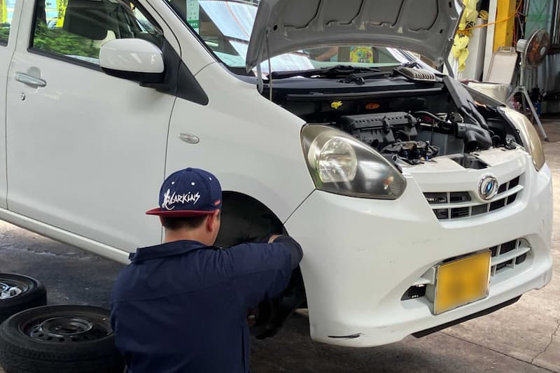 自動車修理工場でボンネットを開けて車両整備をする作業員