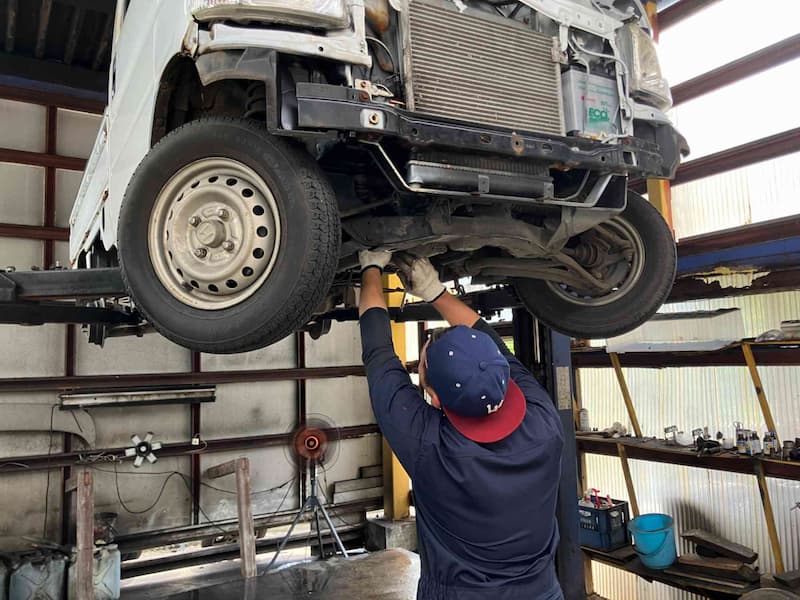 車両整備士がリフト上の車両の足回りを確認している作業風景