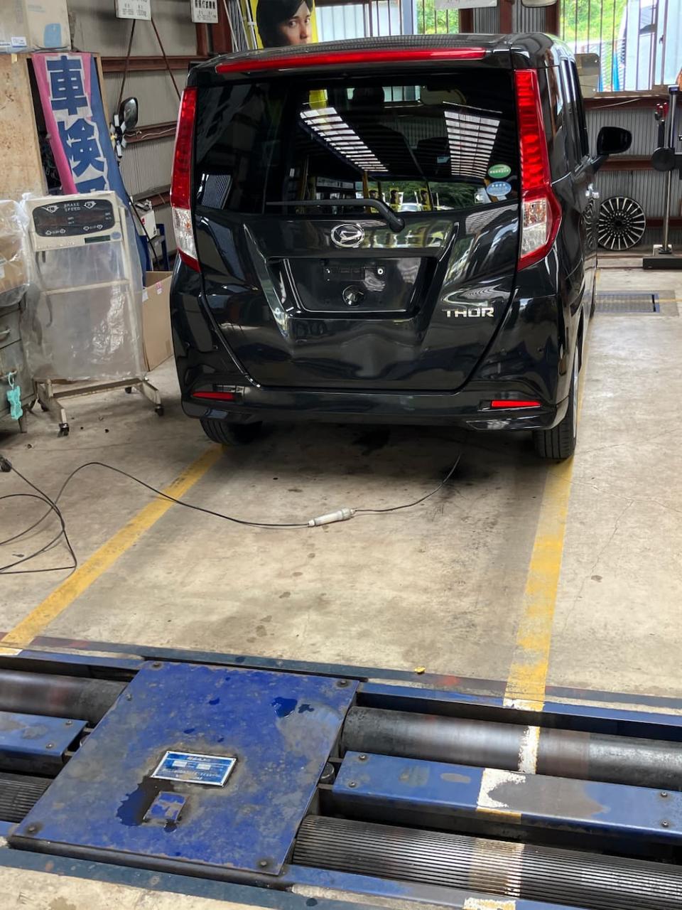 整備工場の検査ピットで車両点検を受ける黒いコンパクトカー