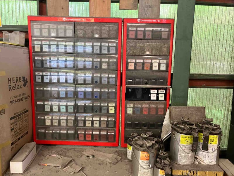 整備工場内にあるカラー塗料の棚に陳列された各色のスプレーペイントと塗料缶