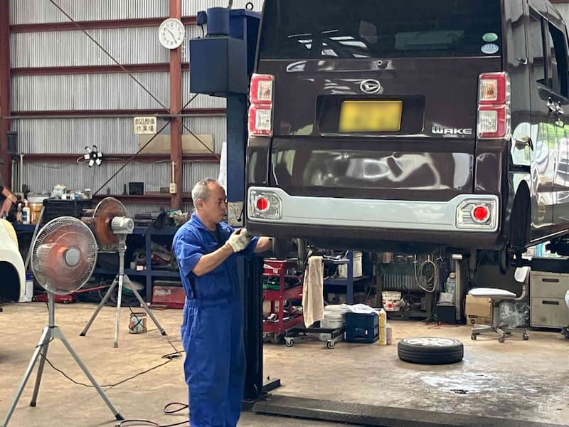 青い作業着を着た整備士がリフトアップされた車を整備している様子